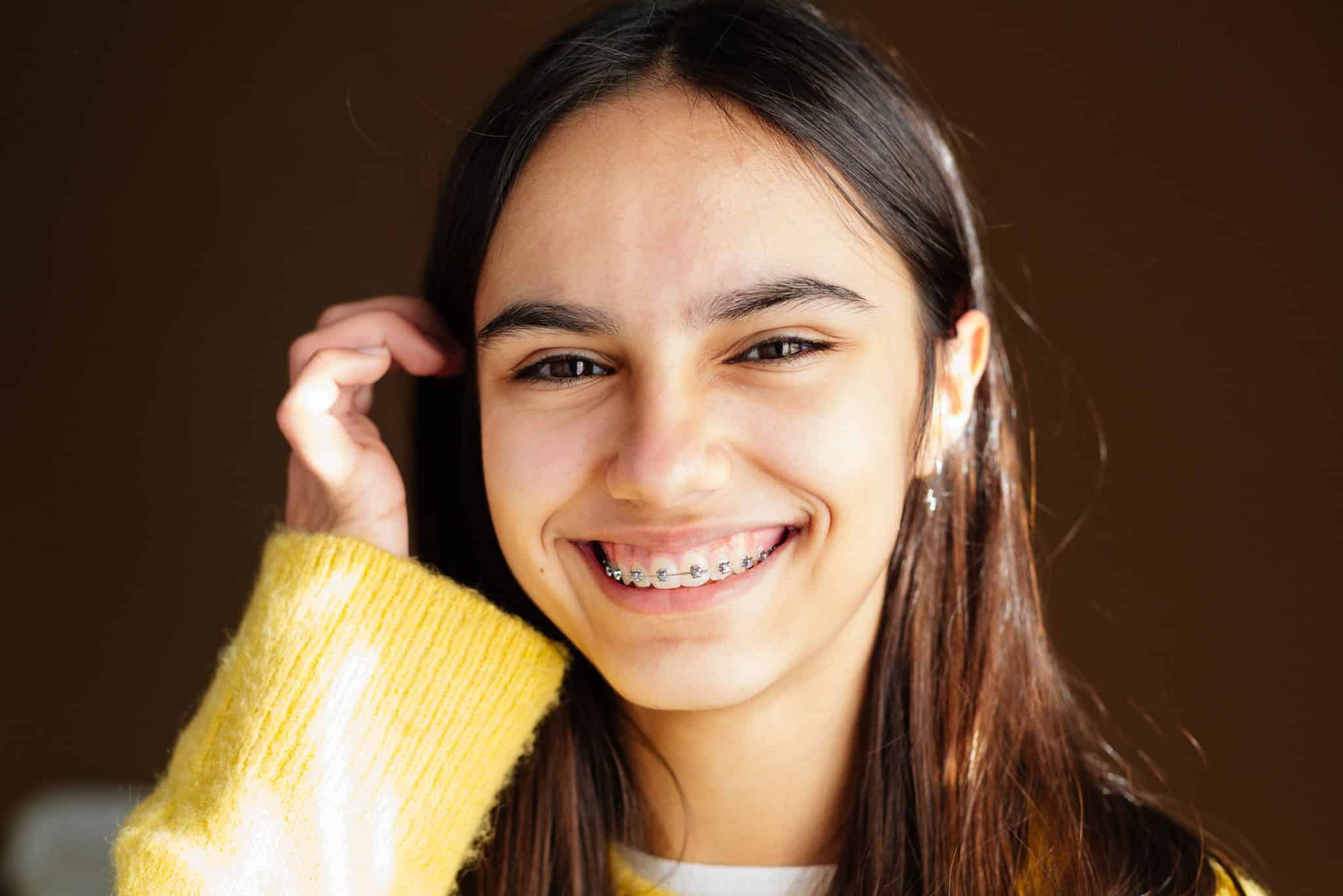 A photo of a woman with traditional metal braces wearing a yellow sweater