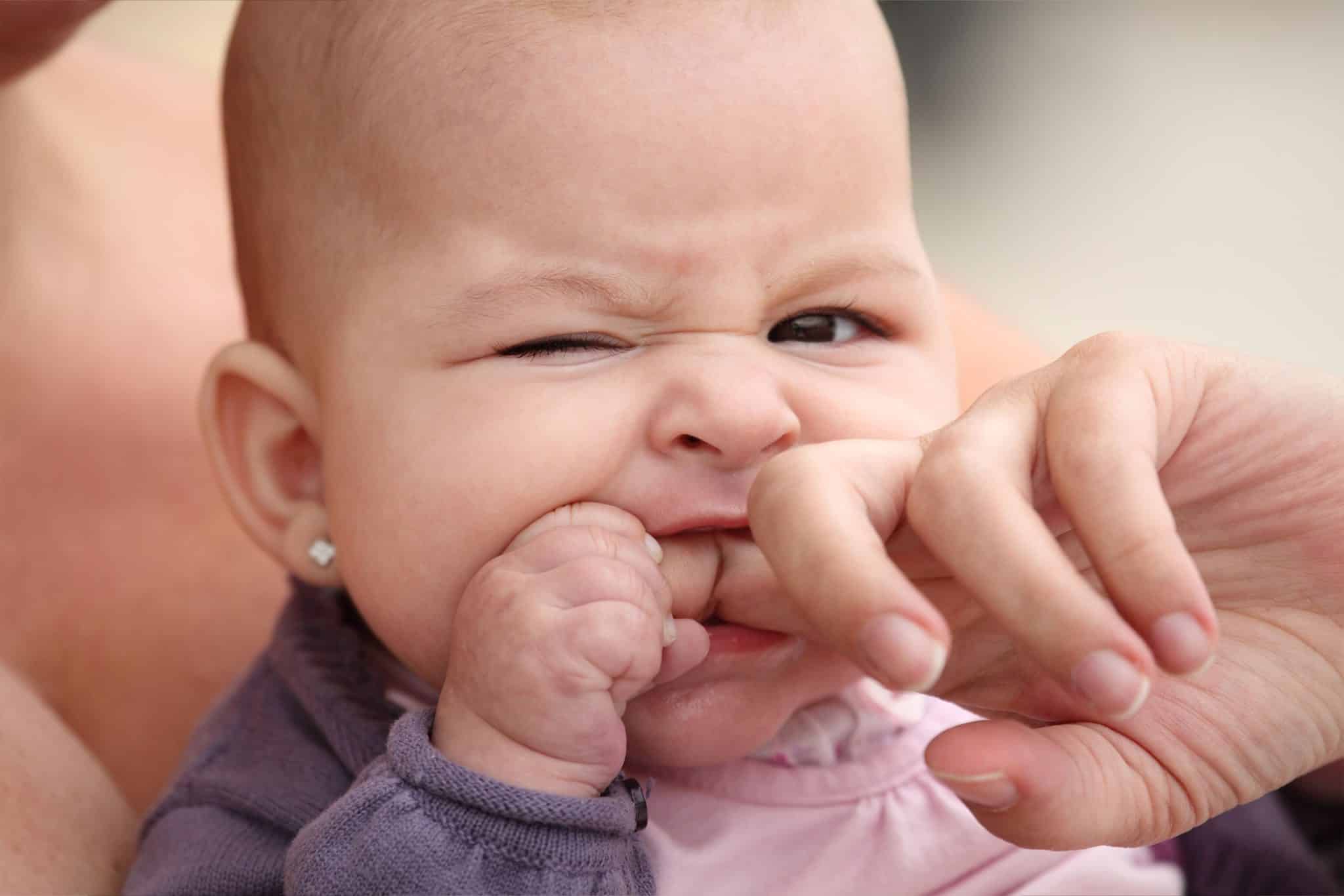 Photo of a teething baby biting a parent's hand