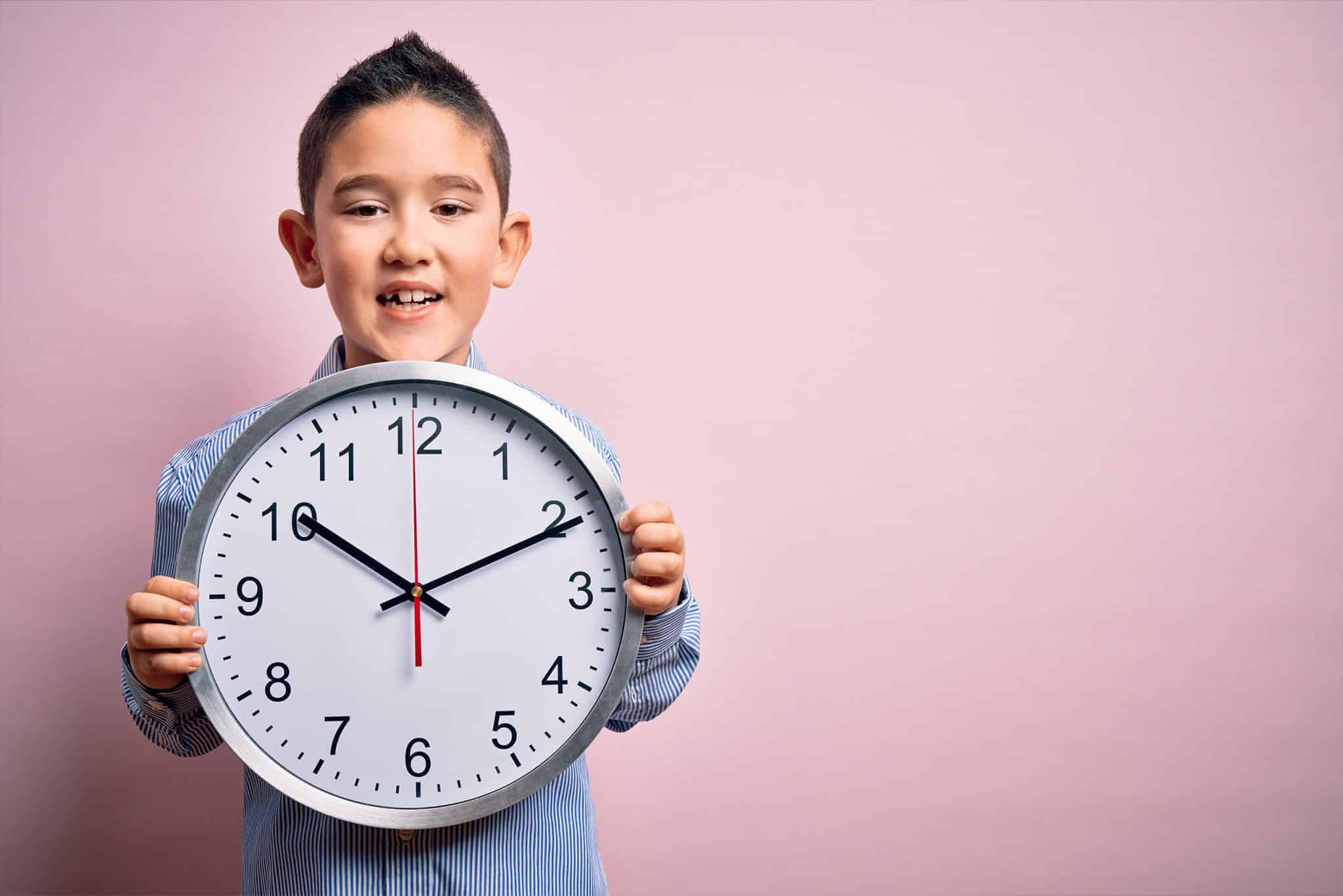 a little boy holding up a large analog clock