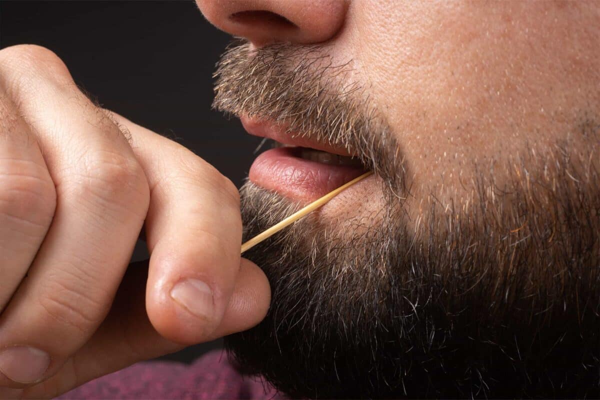 A man cleaning his teeth with a toothpick.