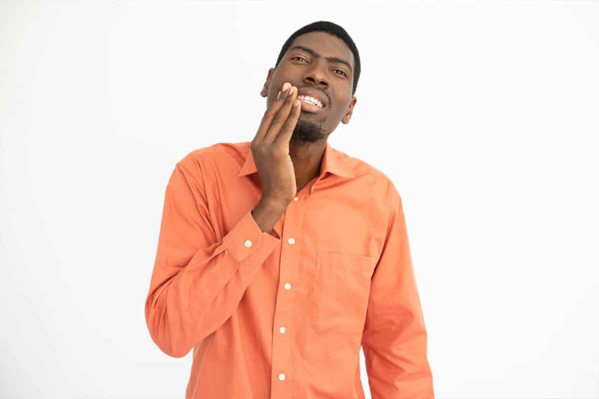 A man in an orange shirt touching his cheek because of his jaw pain.