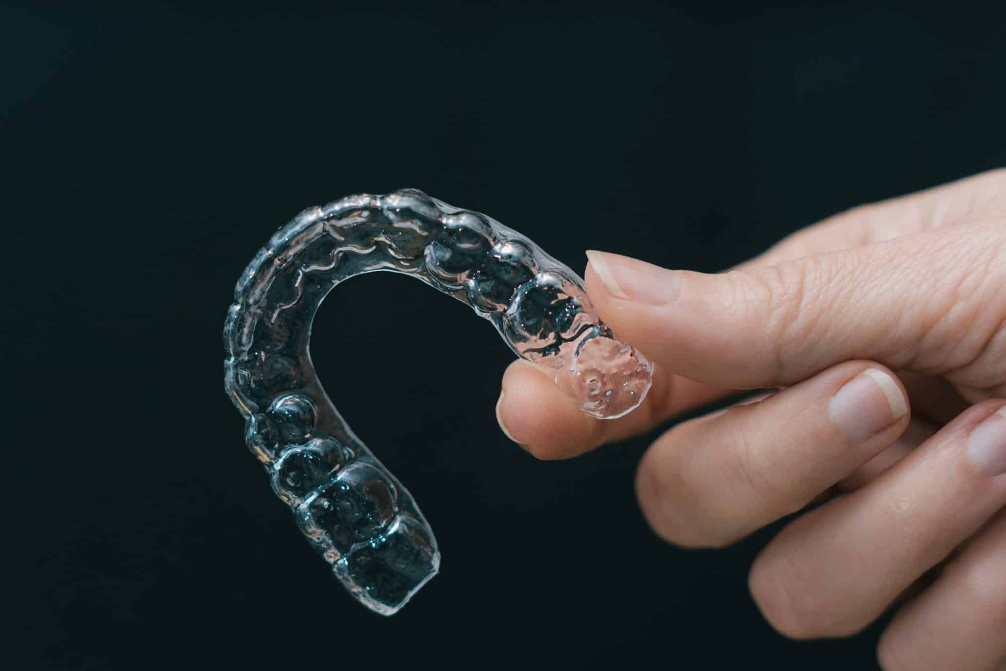 A person holding up a clear aligner, which is an orthodontic device for straightening teeth.