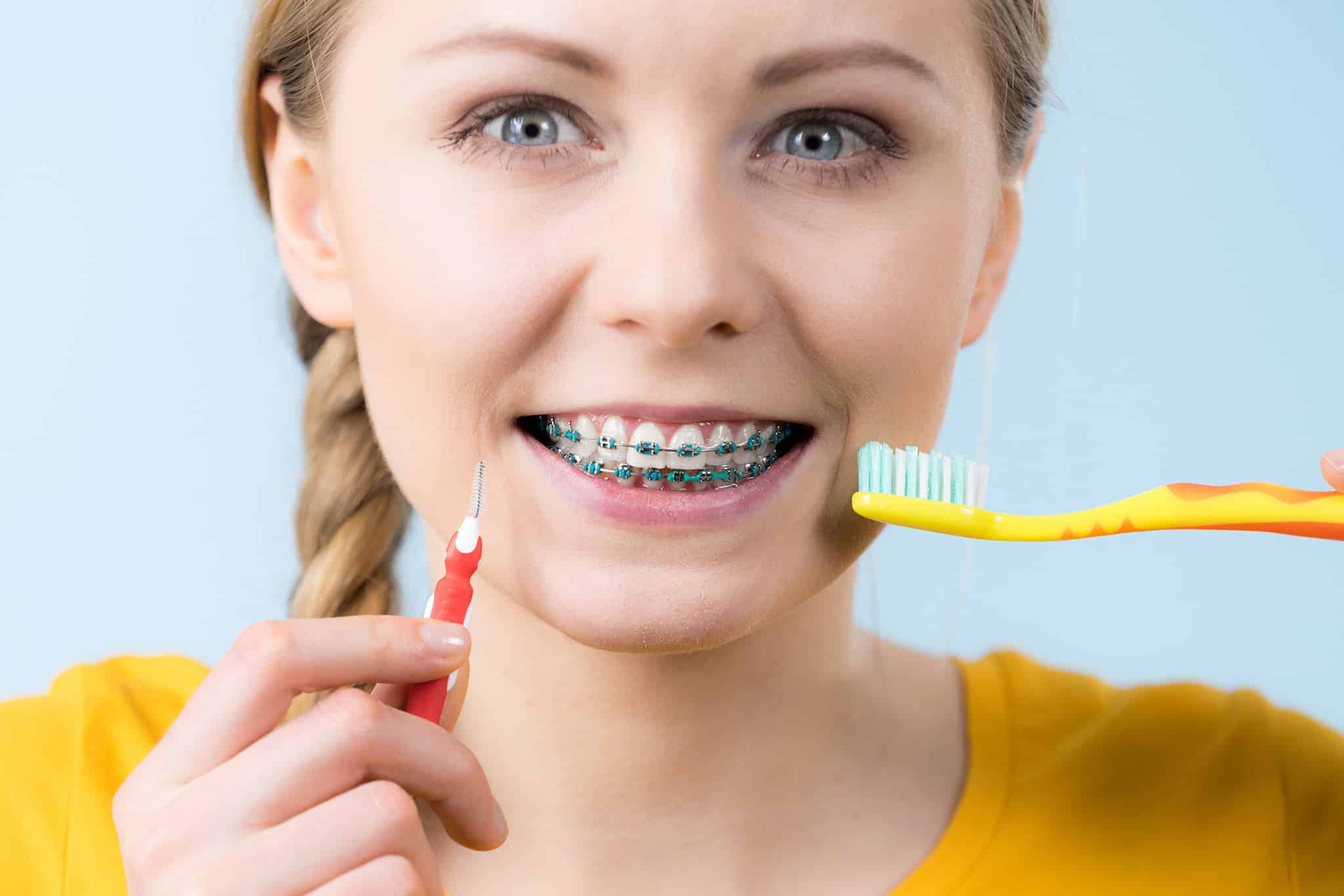 A photograph of a girl with braces holding a toothbrush and dental pick.